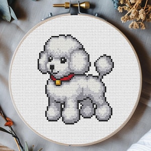 May include: A cross-stitch embroidery hoop showing a white poodle with a red collar and gold tag. The dog is rendered in a pixelated style, set against a white fabric background. The wooden hoop is secured with a brass screw.