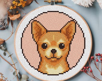 以下が含まれることがあります： チワワ犬の肖像画が描かれたクロスステッチ刺繍枠。犬は茶色、タン、クリーム色で、ピンク色の背景に描かれています。木製の枠は、装飾的な花と葉で囲まれています。