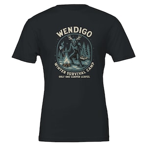 Könnte beinhalten: Schwarzes T-Shirt mit einer Grafik eines Wendigo mit Geweih, der eine Axt und ein Buch hält, in der Nähe eines Lagerfeuers in einem Wald. Der Text lautet "WENDIGO WINTER SURVIVAL CAMP ONLY ONE CAMPER LEAVES."