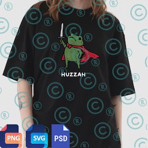Könnte beinhalten: Schwarzes T-Shirt mit einem Cartoon-Frosch-Design. Der grüne Frosch trägt einen roten Umhang und hält ein Schwert. Das Wort "HUZZAH" ist darunter gedruckt. Rundhalsausschnitt und kurze Ärmel.