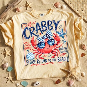 May include: A light yellow t-shirt with a graphic of a red crab wearing sunglasses and a bow tie. The text on the shirt reads "If Crabby, Please Return to the Beach."