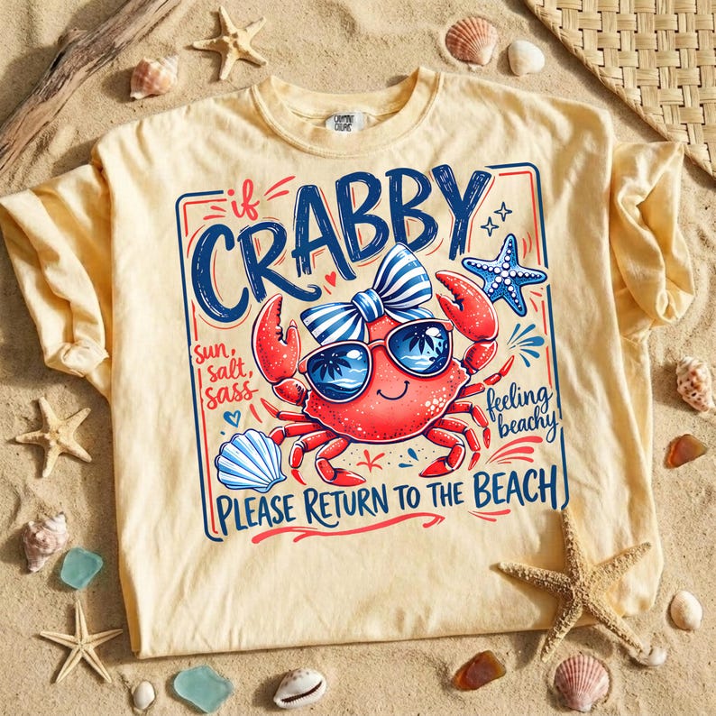 May include: A light yellow t-shirt with a graphic of a red crab wearing sunglasses and a bow tie. The text on the shirt reads "If Crabby, Please Return to the Beach."