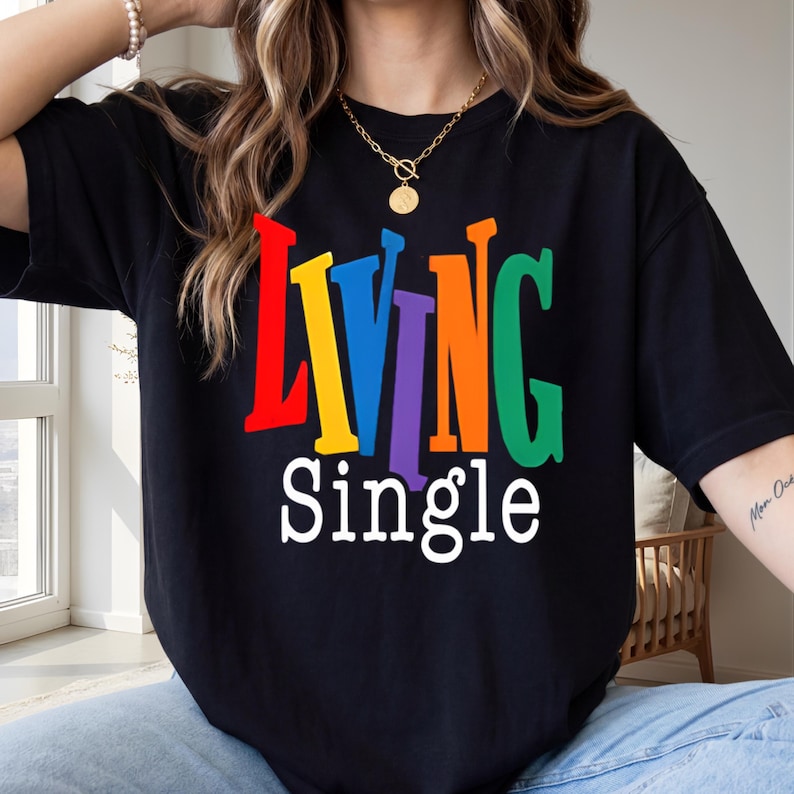 K&ouml;nnte beinhalten: Schwarzes T-Shirt mit dem Schriftzug "LIVING Single" in bunten, regenbogenfarbenen Buchstaben. Ein l&auml;ssiger Stil, geeignet f&uuml;r den Alltag.