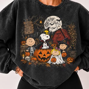 以下が含まれることがあります： ハロウィンの仮装をしたピーナッツのキャラクターのグラフィックプリントが施された、チャコールグレーのミネラルウォッシュスウェットシャツ。スヌーピー、チャーリー・ブラウン、仲間たちがカボチャ、満月、コウモリと共に描かれ、Spooky Friends Make The Best DaysとTrick Or Treatの文字が入っています。