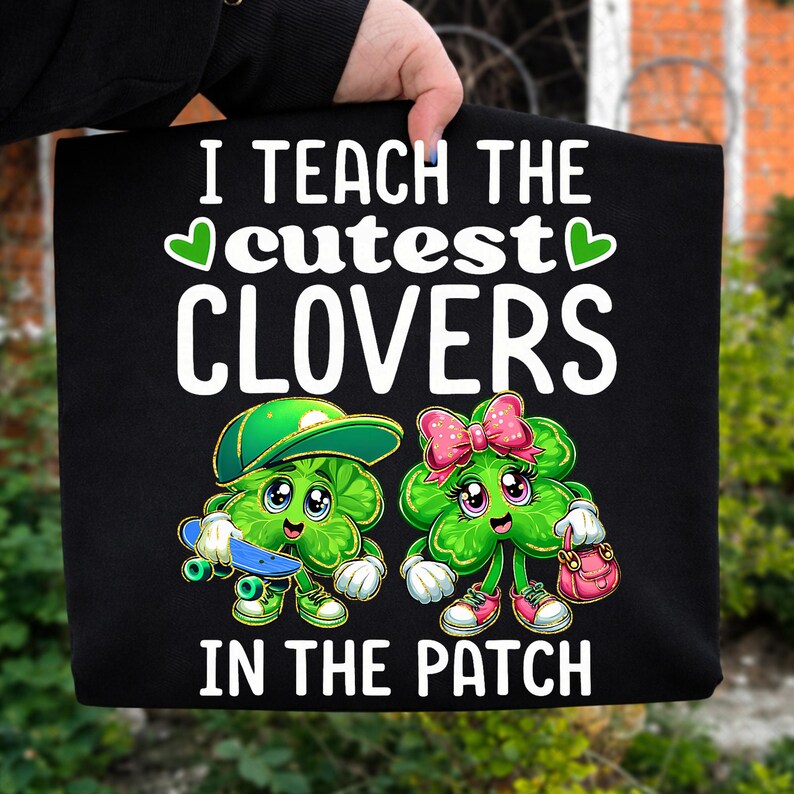 May include: Black sweatshirt with the text "I TEACH THE cutest CLOVERS IN THE PATCH". The graphic features two cartoon clovers, one with a skateboard and the other with a purse. The clovers are green with pink and white accents.