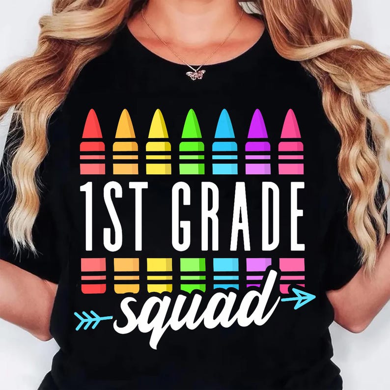 May include: Black t-shirt featuring a colorful crayon design above the words "1ST GRADE squad" in white. The design includes a row of crayons in red, orange, yellow, green, blue, purple, and pink. A fun back-to-school graphic tee.
