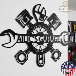 May include: Black metal garage sign with the text "AILIC'S GARAGE" in a cut-out design. The sign features wrenches, pistons, and a gear, with an "American Made" sticker in the lower right corner.