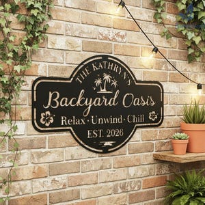 Puede incluir: Letrero de metal negro que dice "The Kathryn's Backyard Oasis" con palmeras y detalles florales. El letrero tambi&eacute;n incluye las palabras "Relax, Unwind, Chill" y "EST. 2026". Est&aacute; montado en una pared de ladrillo.