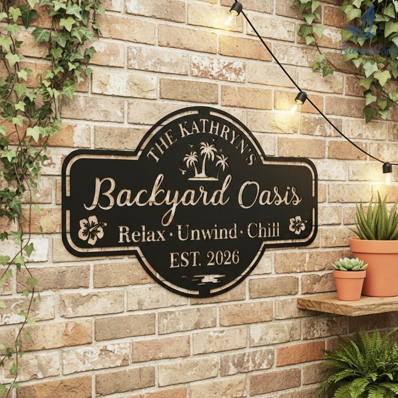 Puede incluir: Letrero de metal negro que dice "The Kathryn's Backyard Oasis" con palmeras y detalles florales. El letrero tambi&eacute;n incluye las palabras "Relax, Unwind, Chill" y "EST. 2026". Est&aacute; montado en una pared de ladrillo.