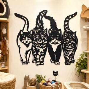 May include: A black metal wall art piece featuring four stylized cats standing side by side. The cats have intricate cut-out details showing various fur patterns and upright tails. The design is flat and mounted directly onto the wall surface.