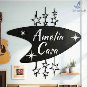May include: Black metal wall art featuring the words "Amelia Casa" in a retro font, with star accents and star-shaped cutouts. The art piece is mounted on a light blue wall, with a guitar and framed artwork visible.