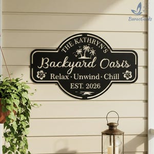 Puede incluir: Letrero de metal negro con la inscripci&oacute;n blanca "The Kathryn's Backyard Oasis". El letrero incluye palmeras y flores, con las palabras "Relax, Unwind, Chill" y "EST. 2026".