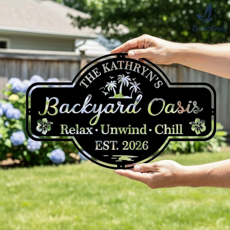 Puede incluir: Letrero de metal negro con el texto "The Kathryn's Backyard Oasis" y las palabras "Relax, Unwind, Chill". El letrero presenta dise&ntilde;os de palmeras y flores de hibisco. El letrero se sostiene frente a un c&eacute;sped verde.