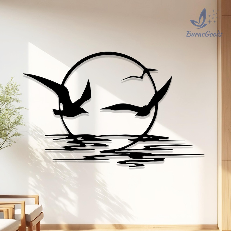 May include: Black metal wall art depicting seagulls flying in front of a sun, with water reflections below. The artwork is mounted on a white wall. The brand name "BuracGoods" is visible in the upper right corner.