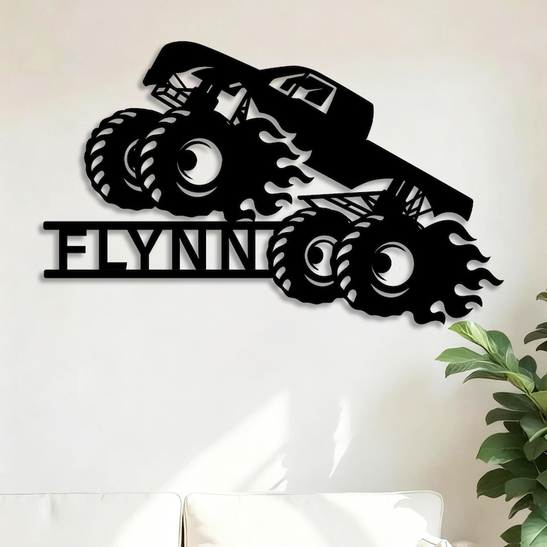 May include: Black metal wall art featuring a monster truck design with large tires and flames. The word "FLYNN" is displayed in bold letters below the truck. The artwork is mounted on a white wall.