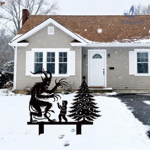 May include: Black metal yard art depicting a Krampus figure menacing a child next to a Christmas tree. The silhouette is mounted on a black bar, set in a snowy yard in front of a house.