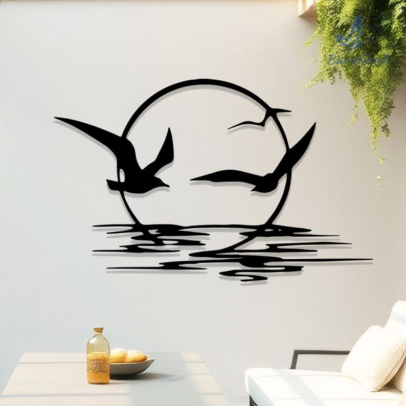 May include: Black metal wall art depicting three birds in flight against a circular sun or moon. Below, stylized lines represent water. The artwork is mounted on a white wall, creating a striking contrast. A decorative piece for home decor.