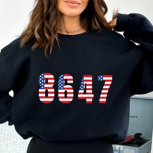 Könnte beinhalten: Schwarzes Sweatshirt mit der Nummer 8647, die in Rot, Weiß und Blau gedruckt ist und der amerikanischen Flagge ähnelt.