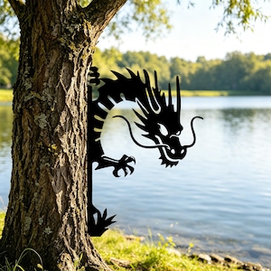 May include: Black metal dragon silhouette garden art. The dragon is positioned as if it is peeking around a tree trunk. The background features a lake and trees.