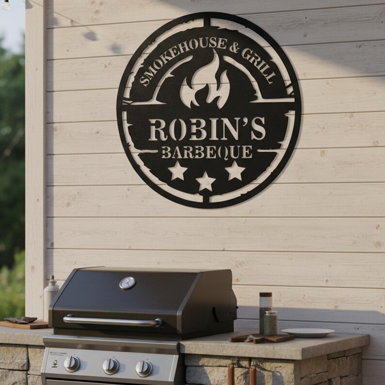 May include: A black metal sign with the words "Smokehouse & Grill" and "Robin's Barbeque" in a circular design, with a flame graphic in the center. Three stars are at the bottom. A black grill is below the sign.