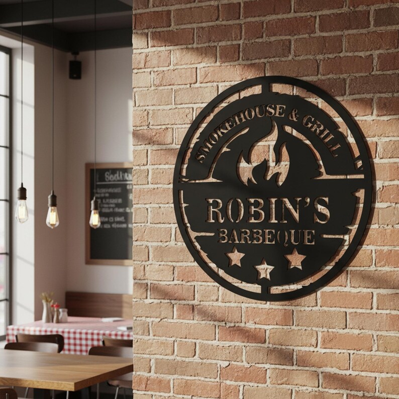 May include: Black metal sign with the words "Smokehouse & Grill" and "Robin's Barbeque" cut out. The sign features a flame design and three stars. It is mounted on a brick wall.