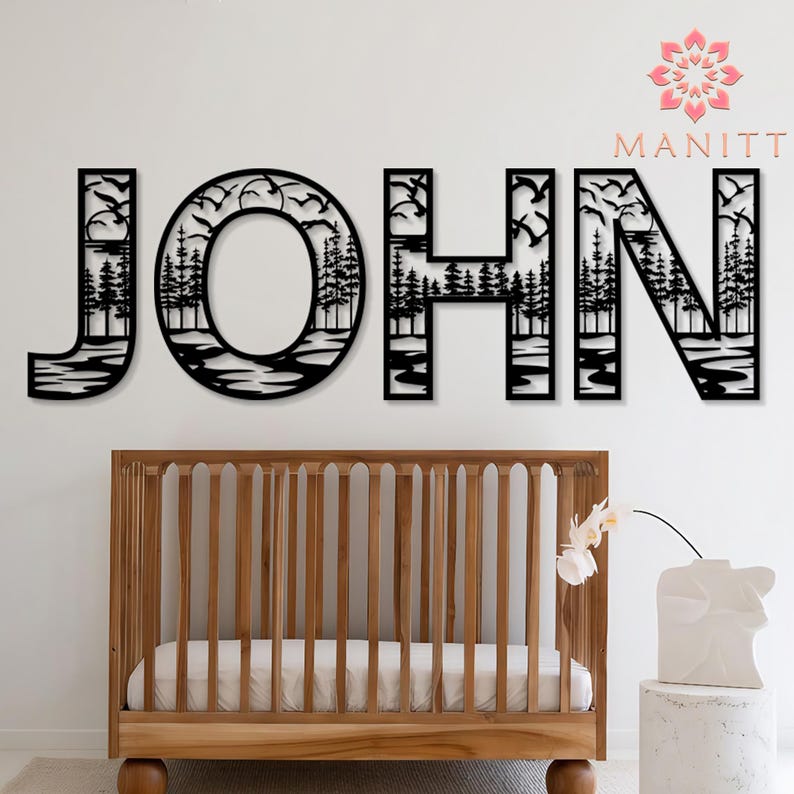 Pode incluir: Arte de parede em metal preto com a palavra "JOHN", apresentando uma cena da natureza com &aacute;rvores e p&aacute;ssaros. As letras s&atilde;o montadas acima de um ber&ccedil;o de madeira com um colch&atilde;o branco. Um vaso branco com uma flor est&aacute; em um pequeno pedestal.