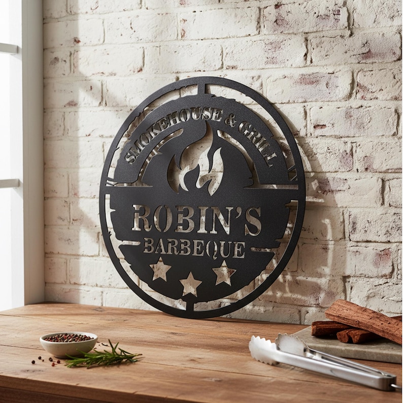 May include: Black metal sign with the text "Smokehouse & Grill" and "Robin's Barbeque" cut out. The sign features a flame design and three stars. It is mounted on a white brick wall.
