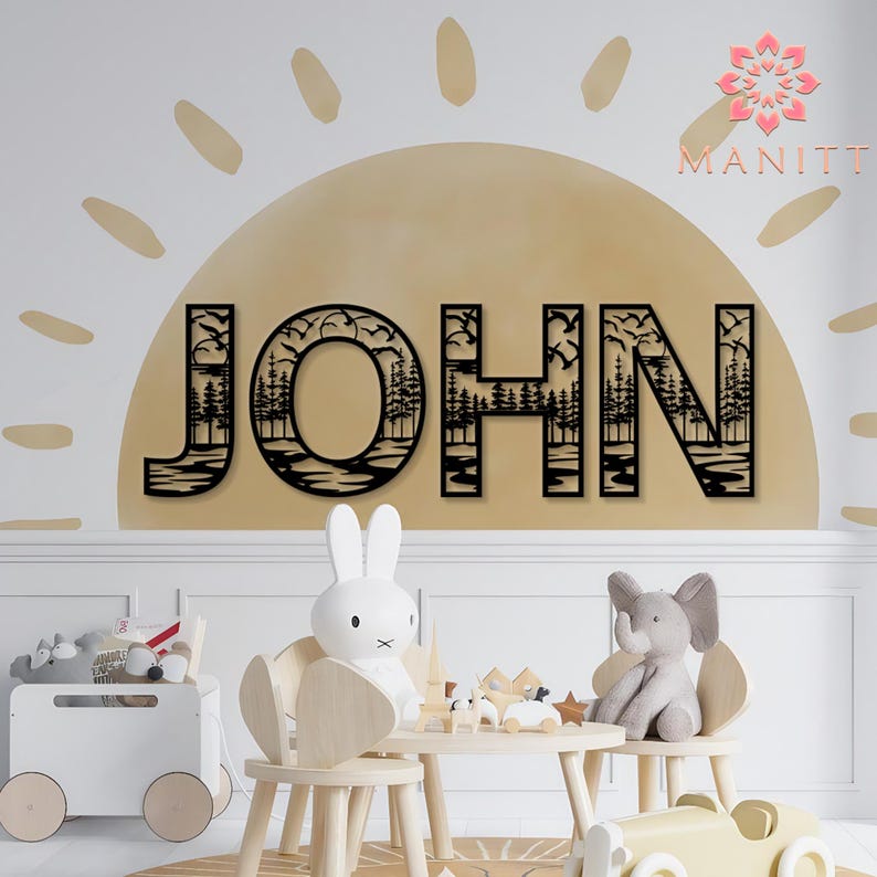 Pode incluir: Arte de parede de madeira preta com a palavra "JOHN" e um design com tema de natureza. As letras apresentam silhuetas de &aacute;rvores, p&aacute;ssaros e &aacute;gua. A arte &eacute; montada em uma parede bege com um design semelhante ao sol, criando um tema decorativo para o quarto das crian&ccedil;as.