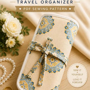 Può includere: Un cartamodello PDF per un organizer da viaggio per gioielli, caratterizzato da una custodia in tessuto beige con stampa floreale mandala blu e gialla, chiusa da un laccio in tessuto abbinato. Il testo recita JEWELRY TRAVEL ORGANIZER PDF SEWING PATTERN.
