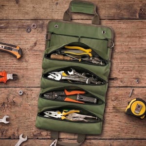 May include: An olive green canvas tool roll organiser featuring four zipped compartments filled with various metal hand tools, including pliers, wrenches, and screwdrivers, with a top carrying handle and metal grommets for hanging storage.