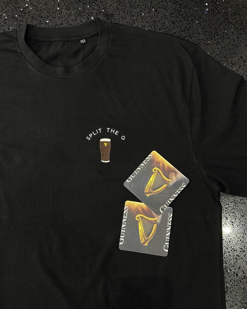 May include: Black t-shirt with the text "SPLIT THE G" and a graphic of a pint of Guinness. Two Guinness coasters are on the shirt.
