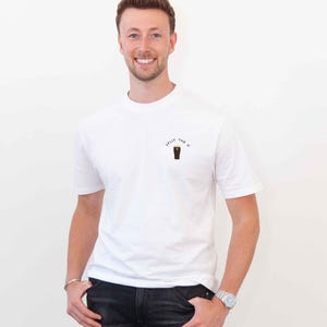 May include: A man wearing a white t-shirt with the text "Split the G" and a graphic of a pint glass. He is wearing black jeans and a silver watch.