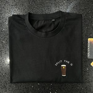 May include: Black t-shirt with white text that reads "Split the G" and a graphic of a pint of Guinness.