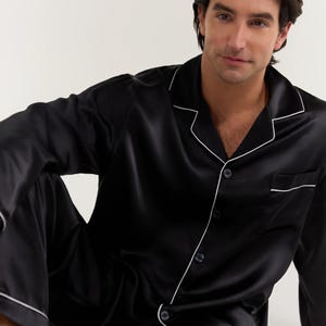 Op de afbeelding: Zwarte zijden pyjama top met witte piping en knoopsluiting.