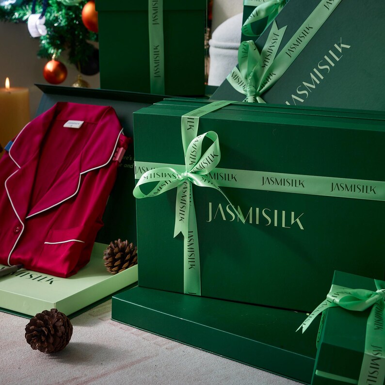 May include: A green gift box with a green ribbon and the text "JASMISILK" printed on it. The box is surrounded by other green gift boxes and a red garment.