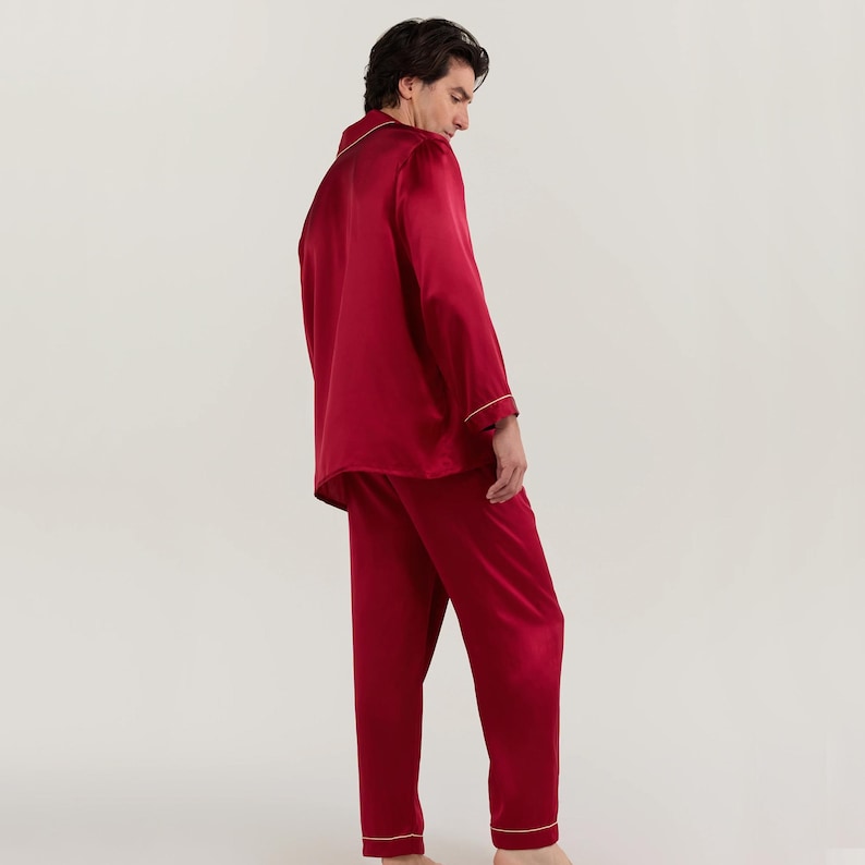 Op de afbeelding: Een rode zijden pyjamaset met een witte bies. Het bovenstuk heeft lange mouwen en een kraag. De broek heeft een rechte pijp.