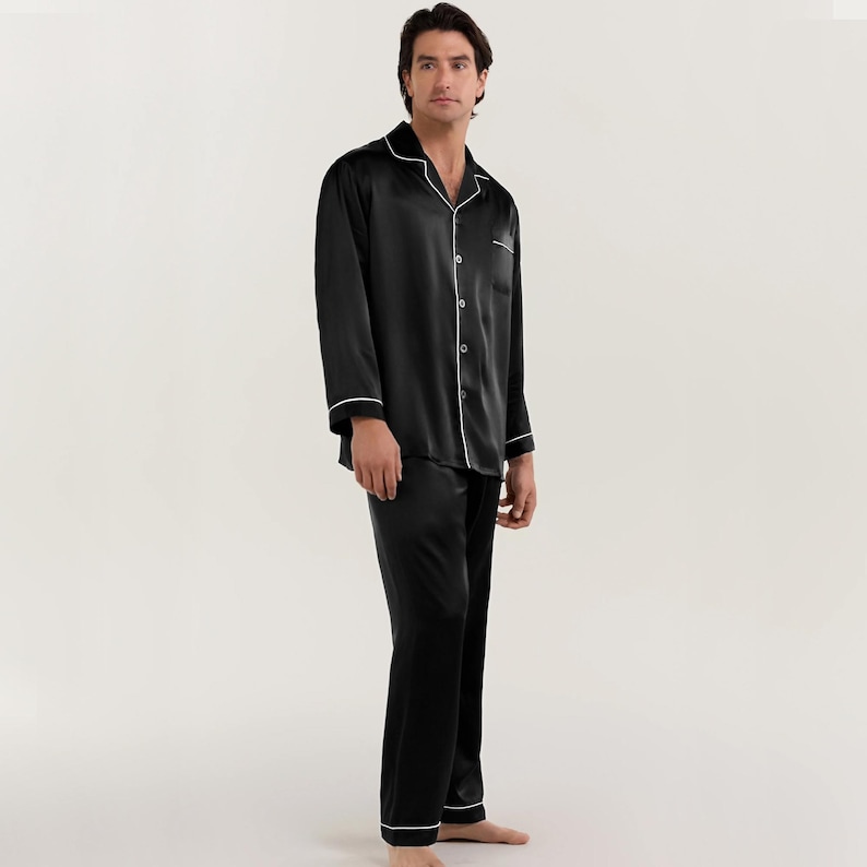 Op de afbeelding: Zwarte satijnen pyjama met witte piping. Het bovenstuk heeft een knoopsluiting en een kraag. De broek heeft een rechte pijp.