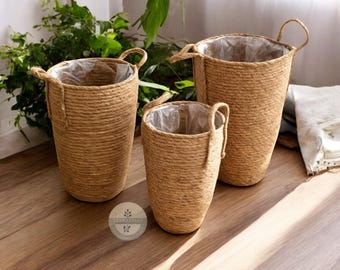 May include: Three brown woven rope plant pots with handles. The pots are different sizes and are arranged in a row on a wooden surface.