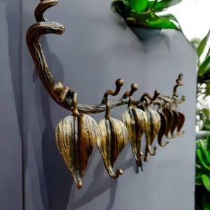 May include: A gold metal wall-mounted coat rack shaped like a branch with leaves. The leaves are designed as hooks.