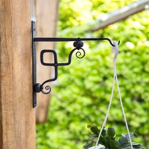The wall-mounted metal bracket for hanging flower pots is handmade by a blacksmith.