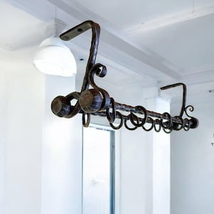Puede incluir: Barra de cortina de metal oscuro y ornamentado con anillos y extremos decorativos. La barra está suspendida del techo y tiene un aspecto rústico y artesanal. El diseño incluye elementos curvos y anillos circulares.