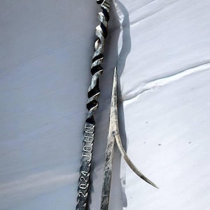 Puede incluir: Dos herramientas de metal plateado sobre un fondo blanco. Una tiene un mango retorcido con un lazo y el texto grabado "2024 JOHN". La otra herramienta tiene un extremo puntiagudo y una hoja curva.