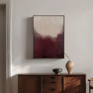May include: Abstract painting in a wooden frame with a gradient of white to burgundy. The painting is hanging on a white wall above a wooden dresser with a vase and bowl on top.