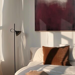 May include: A bedroom with a white bed, brown throw pillow, and a black floor lamp. A painting with a gradient of white to dark red hangs on the wall.