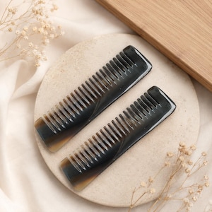 Puede incluir: Dos peines rectangulares para el cabello fabricados en material de cuerno oscuro pulido, con un acabado liso y brillante y variaciones de color naturales en degradado que van del negro carbón profundo a tonos ámbar.
