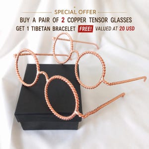 May include: Two pairs of copper tensor glasses with a twisted wire frame design. The text in the image reads: SPECIAL OFFER BUY A PAIR OF 2 COPPER TENSOR GLASSES GET 1 TIBETAN BRACELET FREE! VALUED AT 20 USD. The glasses are resting on a black box.