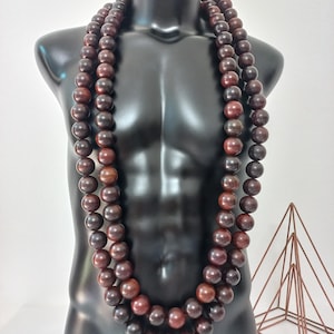May include: A long necklace consisting of two strands of smooth, dark brown wooden beads. The beads are uniform in size and shape, featuring a polished finish that highlights the natural grain and deep reddish-brown tones of the wood material.