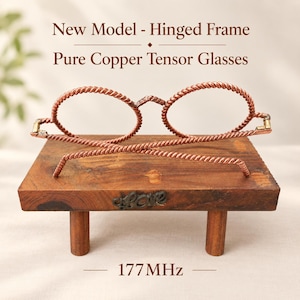 May include: A pair of pure copper tensor glasses with a twisted wire frame and hinged temples, resting on a small wooden stand with four legs. The text New Model - Hinged Frame Pure Copper Tensor Glasses and 177MHz is visible in the image.