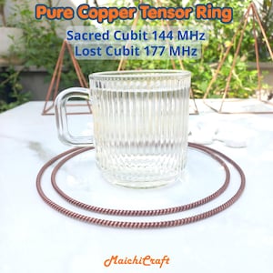 Puede incluir: Una taza de vidrio transparente con estrías verticales se encuentra dentro de dos anillos circulares de alambre de cobre trenzado. El texto en la imagen dice: Pure Copper Tensor Ring, Sacred Cubit 144 MHz, Lost Cubit 177 MHz y MaichiCraft.