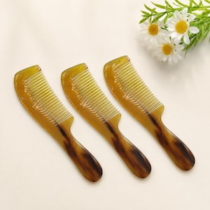Puede incluir: Tres peines para el cabello con un patrón de carey translúcido en tonos ámbar y marrón oscuro. Cada peine tiene un mango redondeado y una serie de dientes finos. Los peines están dispuestos en fila, mostrando un acabado liso y pulido.